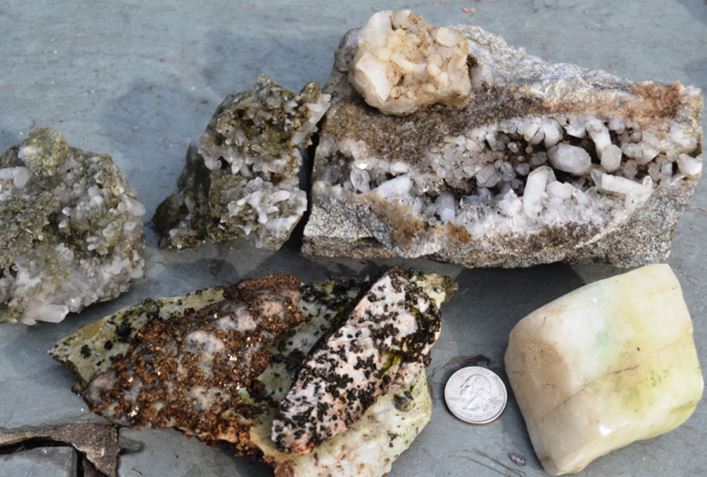 A sampling of rock from Moose River.  The upper row contain quartz crystals.  In the lower left is a piece of bluish marble containing augite.  The etched calcite rhomb was found in the river.